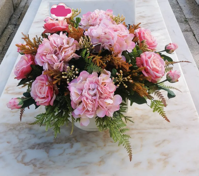 Arranjo de flores artificiais em tons de rosa pousado numa campa de mármore