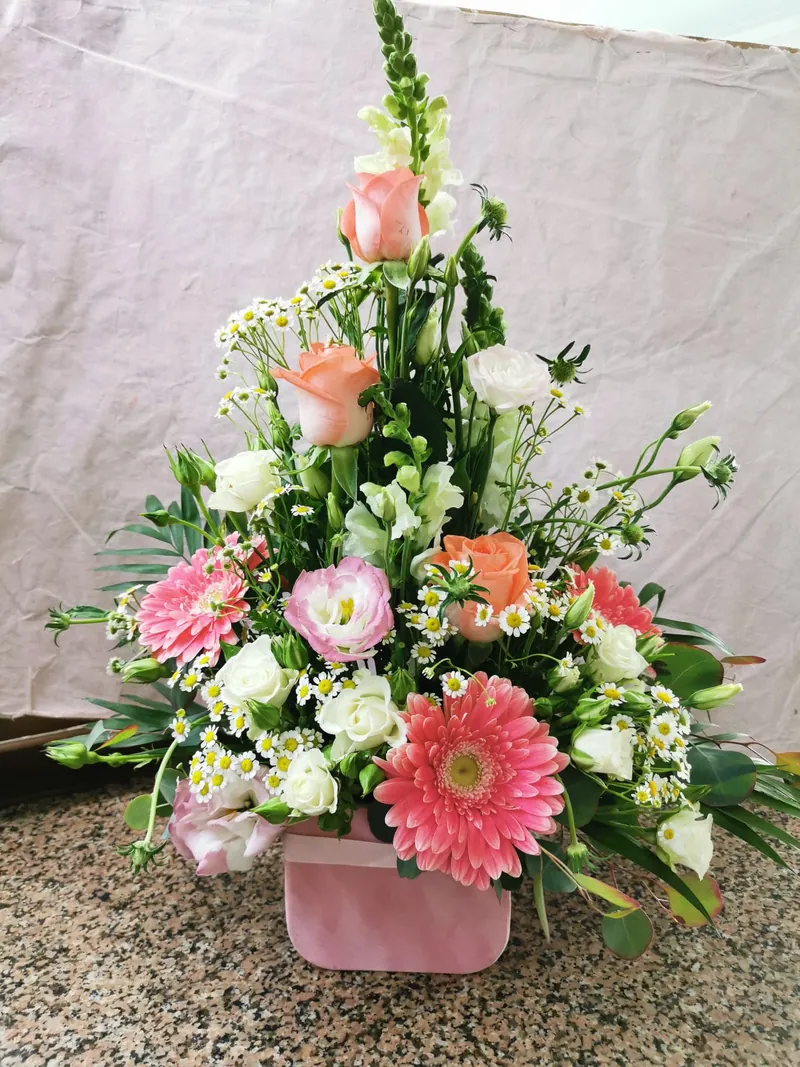 Arranjo alto em caixa cor-de-rosa com gérberas, rosas pêssego e lisianthus branco