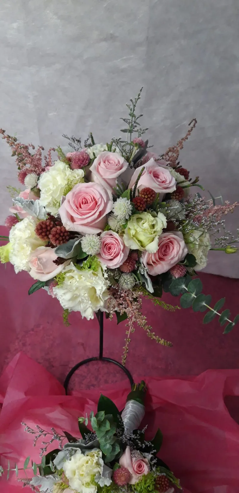 Bouquet de noiva com rosas cor-de-rosa, astilbe e verdes, num suporte da loja