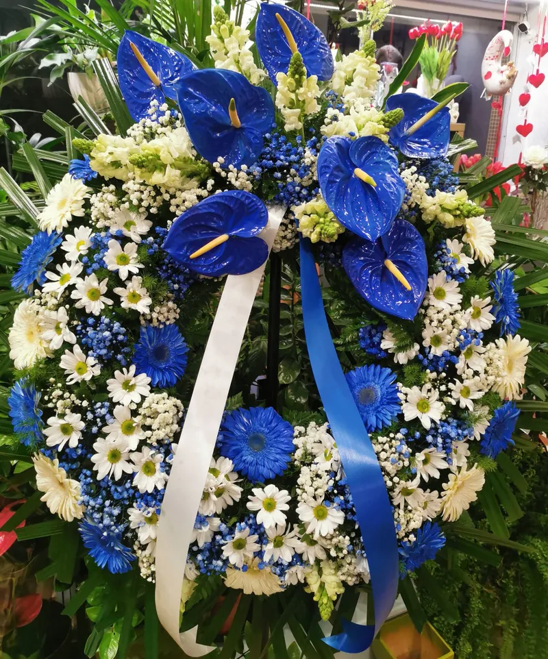 Coroa de funeral em azul e branco, com anthúrios azuis, gérberas e fita azul