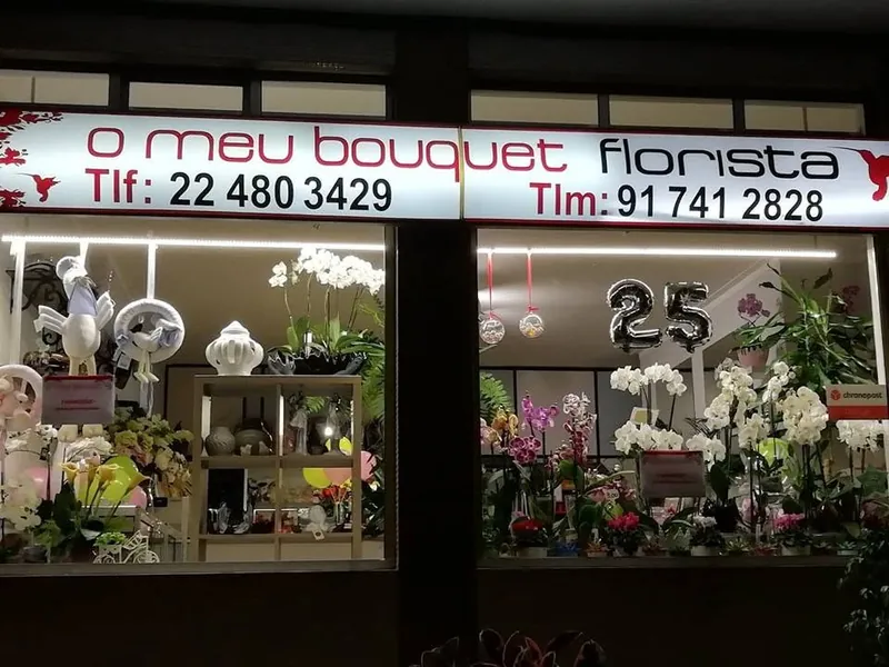 Montra da florista O Meu Bouquet à noite, com o letreiro iluminado e orquídeas na vitrine